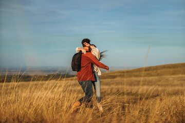 A happy couple is hugging and having a great time on a big golden yellow meadow on a sunny autumn...