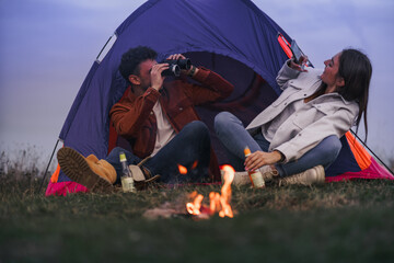 A couple is enjoying camping in nature, a boy is holding binoculars while a girl is taking a photo...