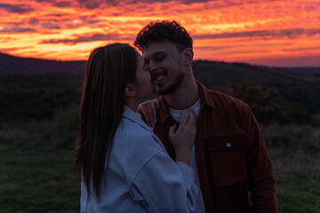 A couple is hugging at breathtaking sunset, surrounded by mountains.