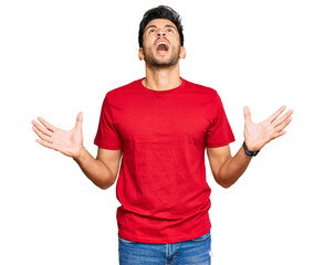 Naklejka premium Young handsome man wearing casual red tshirt crazy and mad shouting and yelling with aggressive expression and arms raised. frustration concept.