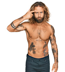 Fototapeta premium Handsome man with beard and long hair standing shirtless showing tattoos pointing unhappy to pimple on forehead, ugly infection of blackhead. acne and skin problem