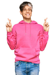 Young hispanic man wearing casual pink sweatshirt gesturing finger crossed smiling with hope and eyes closed. luck and superstitious concept.