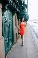 A young girl tourist in a red dress and sunglasses walks down the street. Along the big green doors. historical center of Budapest