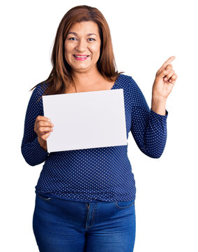 Middle age latin woman holding paper banner with blank space smiling happy pointing with hand and finger to the side