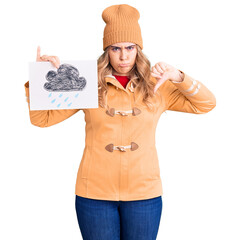 Young caucasian woman wearing winter clothes holding rain draw with angry face, negative sign...