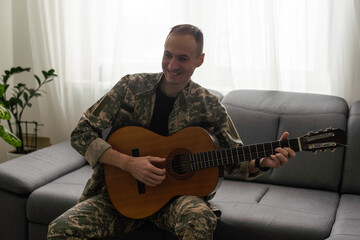 Cheerful smiling young military man wearing khaki uniform holding guitar.