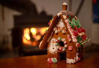 Off center holiday gingerbread house with candy decoration by cozy bokeh fireplace