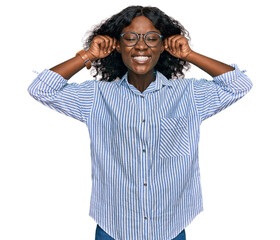 Beautiful african young woman wearing casual clothes and glasses smiling pulling ears with fingers, funny gesture. audition problem