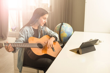 Latin girl with headphones listening to her online music lessons. Artistic kid playing the acoustic...