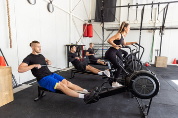 Fototapeta na wymiar Fitness group having high Intensive workout on a bike and on a rowing machine in the industrial gym