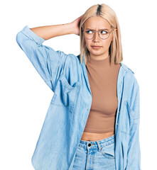 Beautiful young blonde woman wearing glasses confuse and wondering about question. uncertain with doubt, thinking with hand on head. pensive concept.