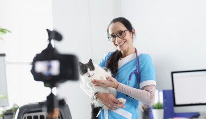Smiling veterinarian doctor demonstrates cat to camera. Pet care and treatment blog concept