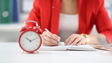 Businesswoman makes notes in documents there is an alarm clock next to it. Time tracking and employee deadlines concept