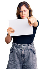Young beautiful caucasian woman holding blank empty paper pointing with finger to the camera and to you, confident gesture looking serious