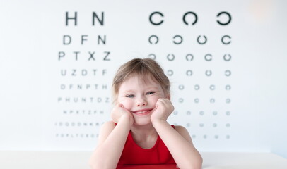 Smiling little child against vision test table in medical clinic portrait. Health and happy...