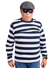 Senior handsome man wearing burglar mask and t-shirt depressed and worry for distress, crying angry...
