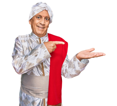 Senior hispanic man wearing tradition sherwani saree clothes amazed and smiling to the camera while presenting with hand and pointing with finger.