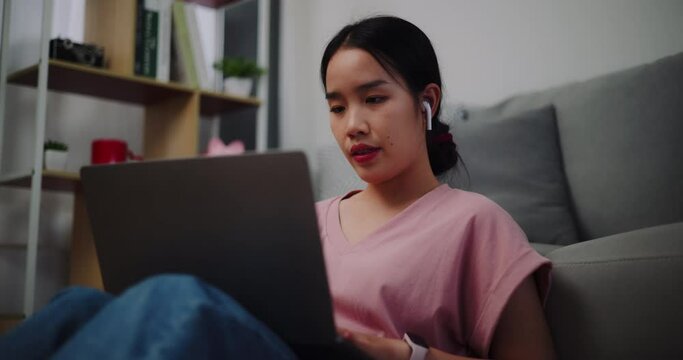 Footage of Young woman sitting on the floor leaning against a sofa working with a laptop and typing work at home office.