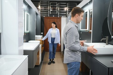 Young family couple choosing bathroom sink in bathroom fixtures store - obrazy, fototapety, plakaty