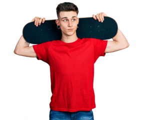 Young caucasian boy with ears dilation holding skate over shoulders smiling looking to the side and staring away thinking.