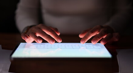 Female fingers are typing on tablet screen at night. People's dependence on modern gadgets concept