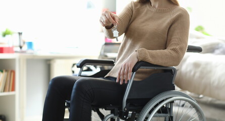 Woman in wheelchair holding apartment key closeup. Social support for people with disabilities...