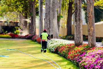Tuinposter Gardener worker watering the flower trees at natural public park. © torjrtrx