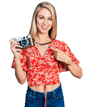Beautiful young blonde woman holding vintage camera smiling happy pointing with hand and finger
