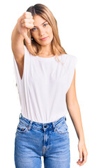 Beautiful caucasian woman with blonde hair wearing casual white tshirt looking unhappy and angry showing rejection and negative with thumbs down gesture. bad expression.