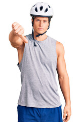 Young handsome man wearing bike helmet looking unhappy and angry showing rejection and negative with thumbs down gesture. bad expression.