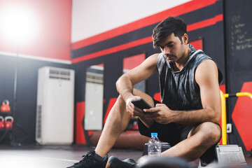 A Caucasian athlete male is talking with his friend by mobile phone before or after exercise in gym...