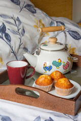 Closeup of tray with teapot, cup and muffins for breakfast in bed, vertical, with copy space