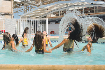 Group of eight teenage girls shaking their hair in the pool after synchronized swimming class.
