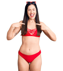 Young beautiful caucasian woman wearing bikini looking confident with smile on face, pointing...