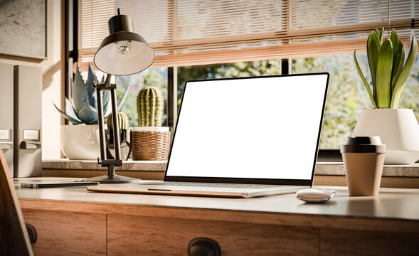 A laptop with a blank screen sits on a stylish wooden desk within a loft-style interior, with green spaces in the background visible through the window. 3d render