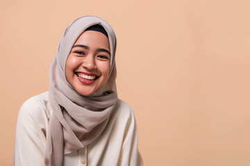 Beautiful Asian young Muslim woman wearing hijab, smiling and looking at camera on beige background