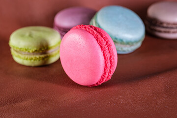Strawberry macaron in the foreground. Colorful macaron candies on leather. Selective focus.