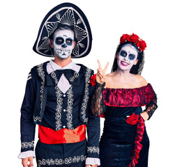 Young couple wearing mexican day of the dead costume over background showing and pointing up with fingers number two while smiling confident and happy.