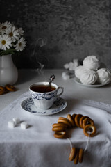 Freshly brewed black tea in a traditional cup with a steam on a grey background with sugar cubes, flowers, zefir and sushki. Russian tea ceremony