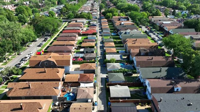 Chicago suburb with rows of brown-roofed houses and green yards in summer. Aerial flight above urban sprawl, backyards in neighborhood.