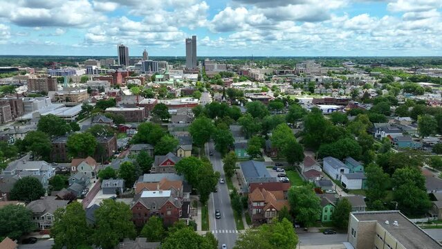 Fort Wayne during summer day. Aerial truck shot of neighborhood and skyline. Green trees, houses, blue sky, and tall skyscrapers in Indiana city.