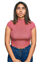 Young hispanic girl wearing casual t shirt making fish face with lips, crazy and comical gesture. funny expression.