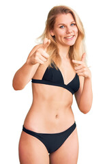 Fototapeta premium Young beautiful blonde woman wearing bikini pointing fingers to camera with happy and funny face. good energy and vibes.