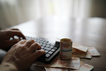 Stacks of 5000 ruble banknotes on the table next to the laptop. Savings and investments in the conditions of sanctions and inflation. - obrazy, fototapety, plakaty
