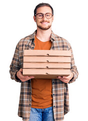 Young handsome caucasian man holding delivery pizza box looking positive and happy standing and...