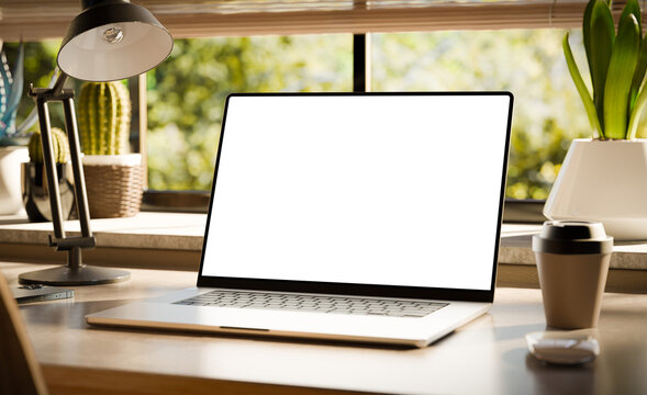 A laptop with a blank screen sits on a stylish wooden desk within a loft-style interior, with green spaces in the background visible through the window. Transparent screen - 3d render