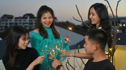 Group of cheerful young people having fun during a rooftop party while toasting with alcohol.