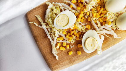 Chopped Peking cabbage, peeled eggs and yellow canned corn on cutting board as a background. Cooking a healthy eco-friendly salad from natural products. Copy space and place for text