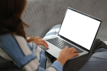 Cropped shot young woman using laptop on comfortable couch at home. Blank screen for advertising.