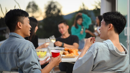 Happy friends having fun at outdoor rooftop party and chatting. Holiday celebration and friendship concept.